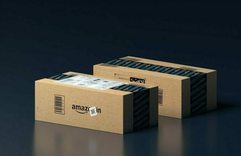 Two Amazon shipping boxes with branded tape and labels are placed on a reflective surface against a dark background.